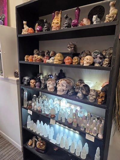 Black wall shelving displaying carved crystal skulls, polished spheres, selenite towers, and oracle decks
