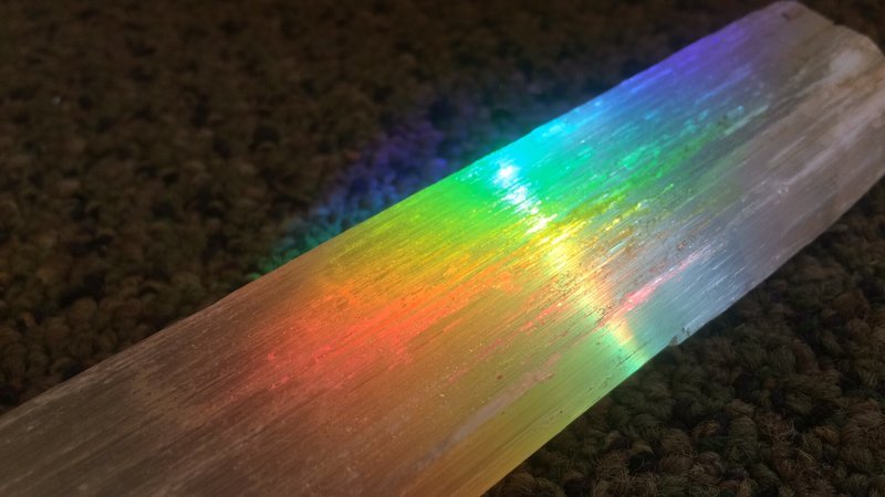 Rainbow iridescent selenite crystal wand displaying spectrum of colors