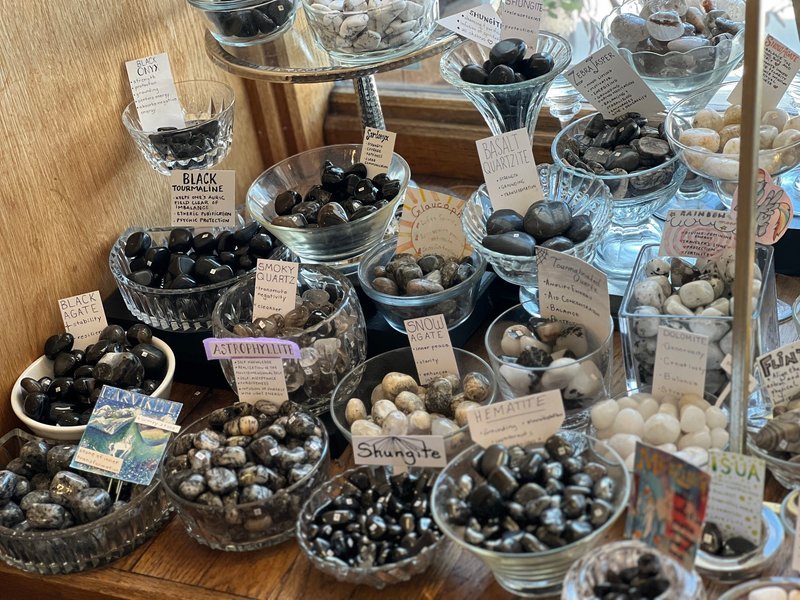 Organized display of tumbled stones in glass bowls sorted by type with labels