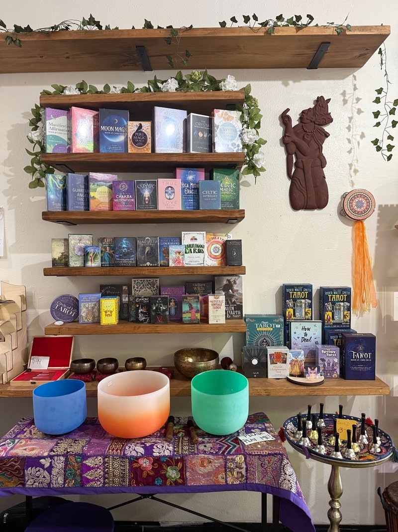 Wooden shelves displaying tarot decks, oracle cards, spiritual books, and singing bowls